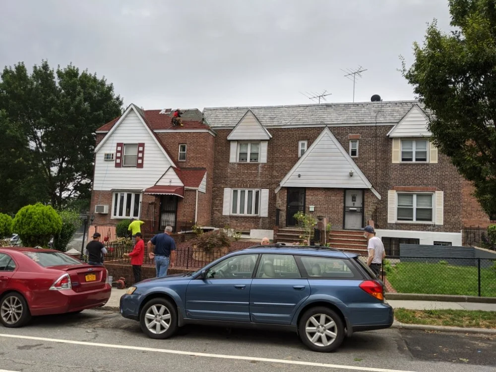 Roofing crew working on top of a residential brick townhouse while people watch from the street below