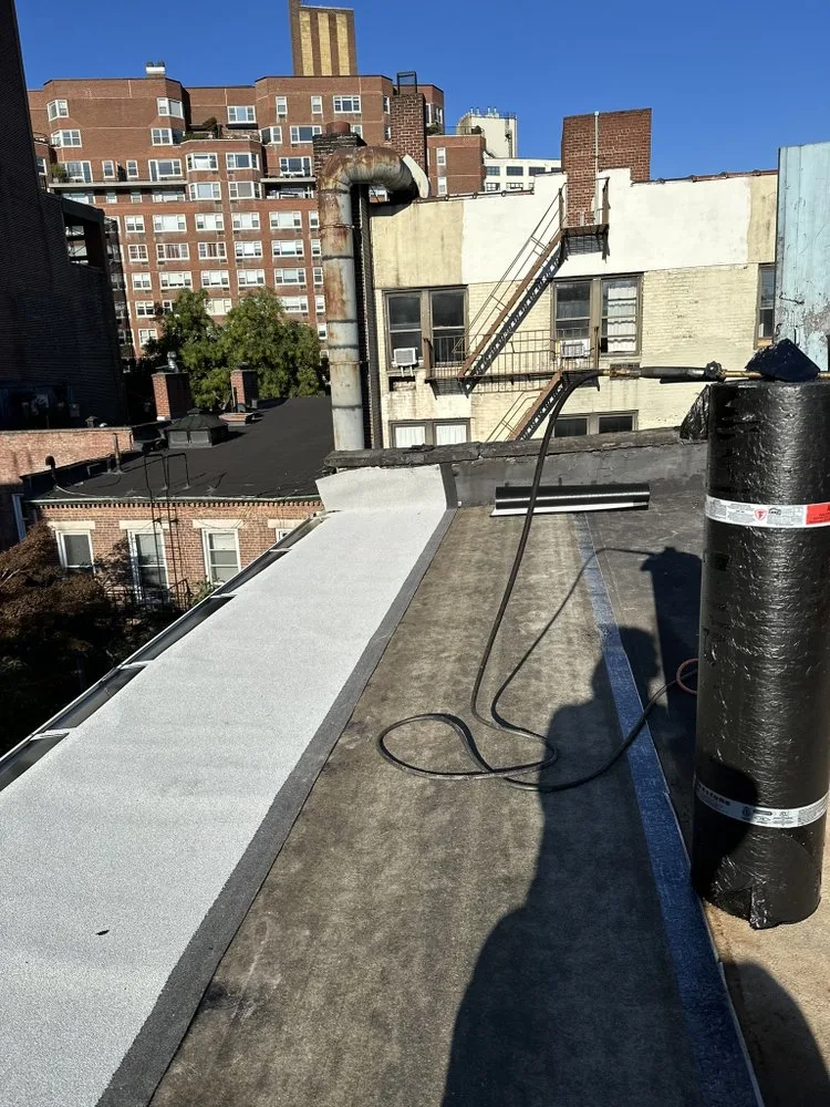 Flat rooftop under repair with new protective coating applied, showcasing professional roofing services in an urban residential area.