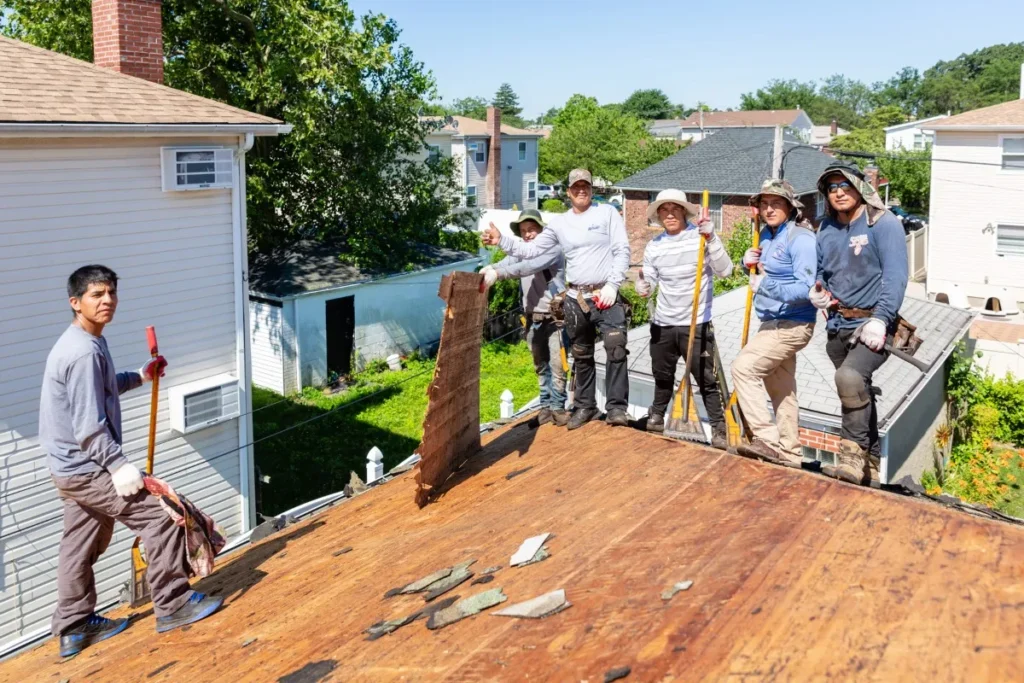 Team of roofers standing on a residential rooftop with tools, preparing for repair and installation as part of professional roofing services.