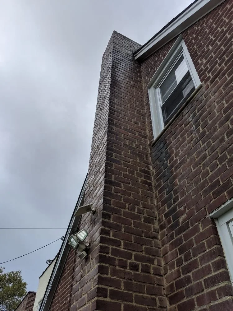 Close-up view of a brick chimney on a residential house, showing aging masonry and water stains along the structure.
